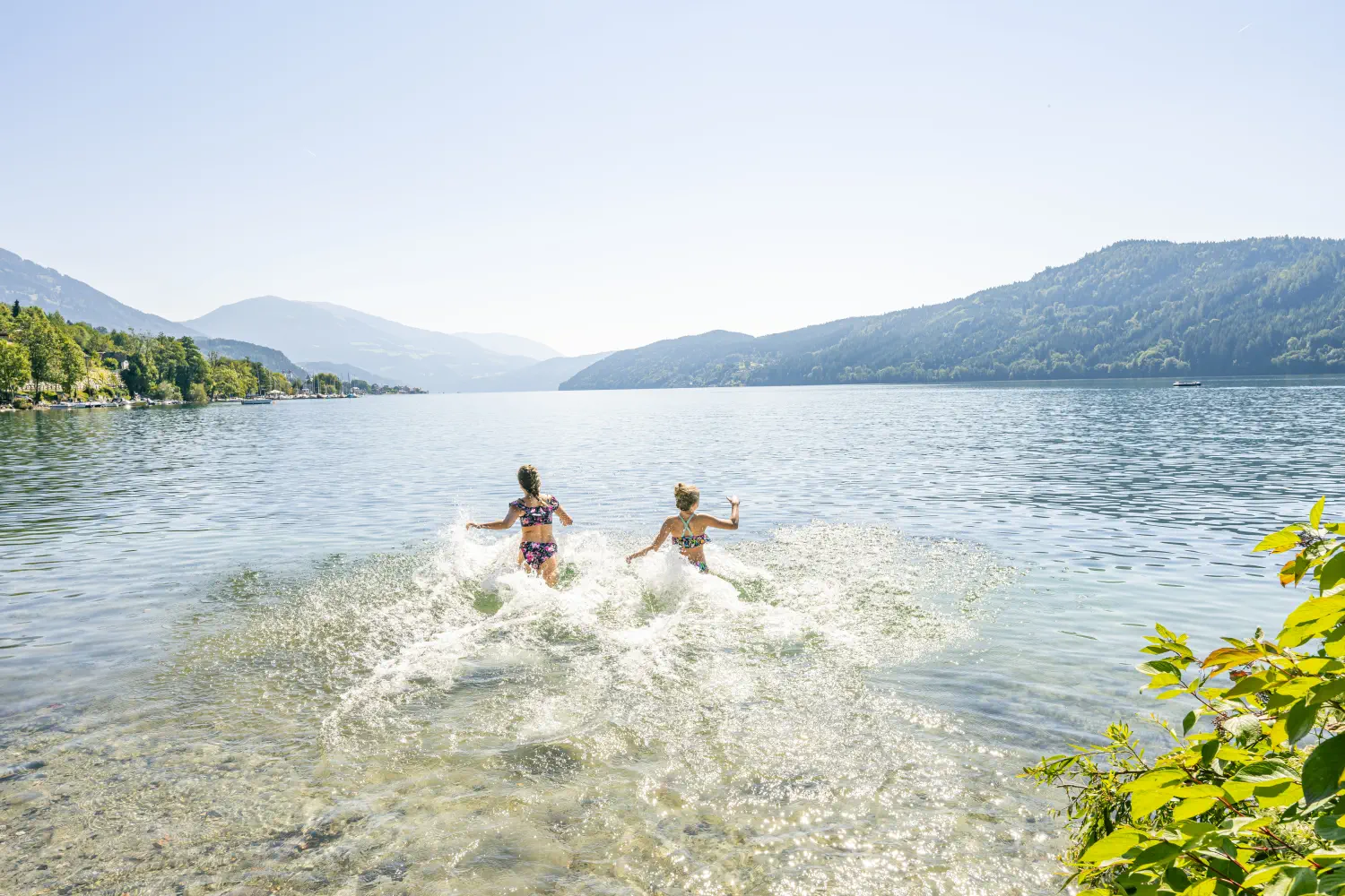 Zwei Mädchen laufen im Sommer voller Freude in den warmen Millstätter See zum Schwimmen