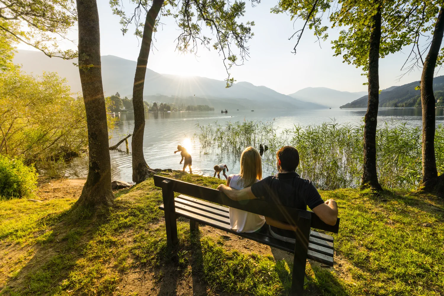 Eine Familie genießt den Sonnenuntergang am Millsätter See. Die Kinder spielen am Wasser.